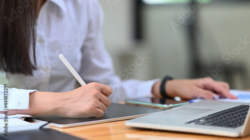 Female office worker holding stylus pen writing information on digital tablet.