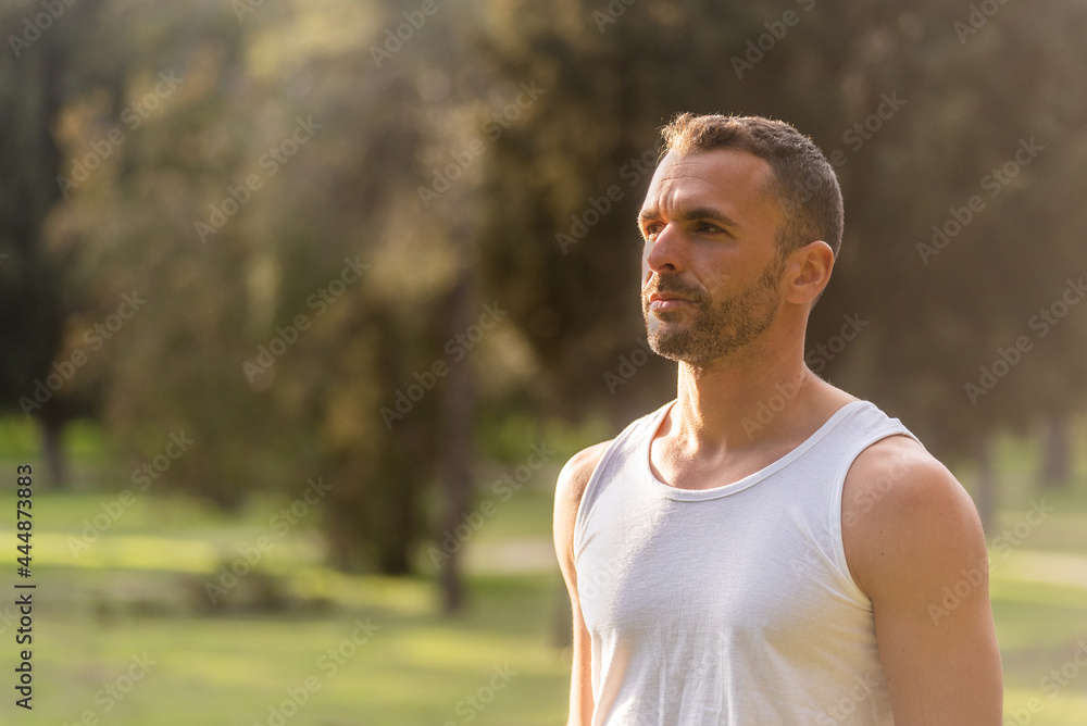 Close-up of an adult man wearing white top tank looking away in the park