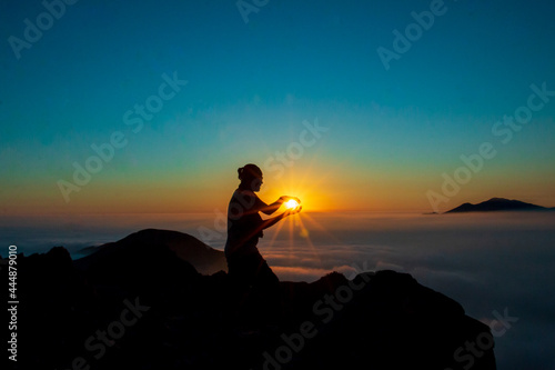 Silhouette of a man touching the sun with both hands on top of a mountain. sunset and cloud sky background.