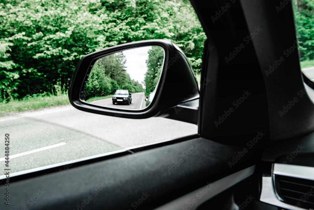 Moving car in side rear-view mirror of modern car.