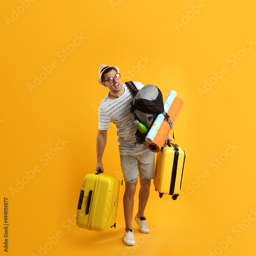 Male tourist with travel backpack and suitcases on yellow background