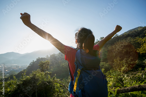 Cheering young woman hiker open arms on mountain peak