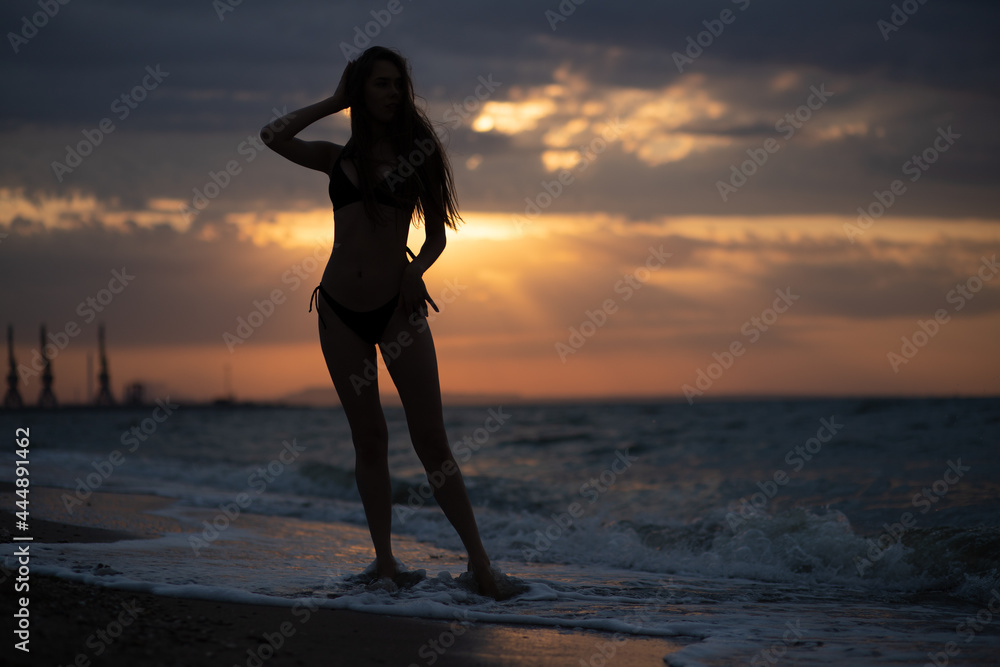 Young girl walks on the sea coast at sunrise. Silhouette photography.