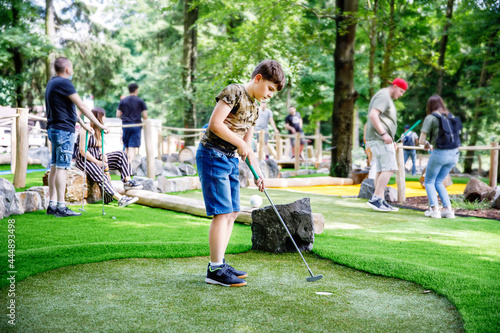 School kid boy playing mini golf with family. Happy child having fun with outdoor activity. Summer sport for children and adults, outdoors. Family vacations or resort.