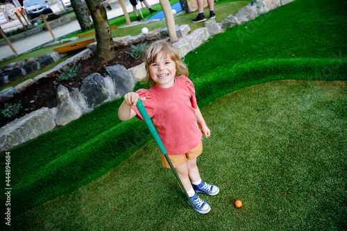 Cute preschool girl playing mini golf with family. Happy toddler child having fun with outdoor activity. Summer sport for children and adults, outdoors. Family vacations or resort. photo