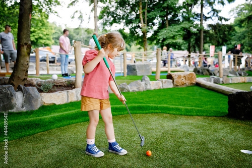 Cute preschool girl playing mini golf with family. Happy toddler child having fun with outdoor activity. Summer sport for children and adults, outdoors. Family vacations or resort. photo