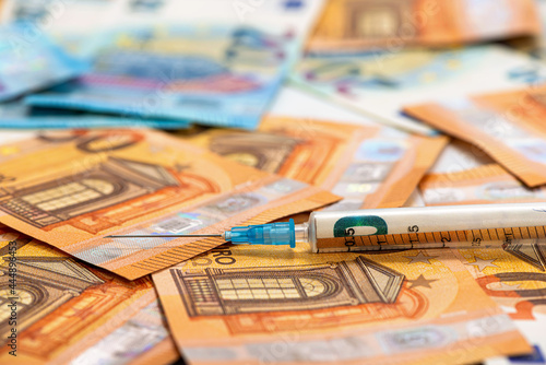 spread stack of Euro banknotes with syringe on top of them, health costs concept
