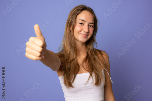 Young smiling woman showing thumb up isolated over purple background.