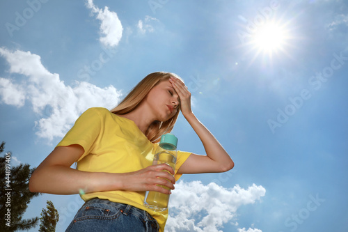 Woman with bottle of water suffering from heat stroke outdoors photo