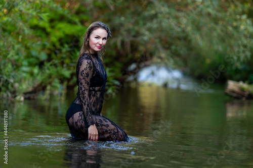 Fototapeta Naklejka Na Ścianę i Meble -  woman in a dark lace dress splashes in the river