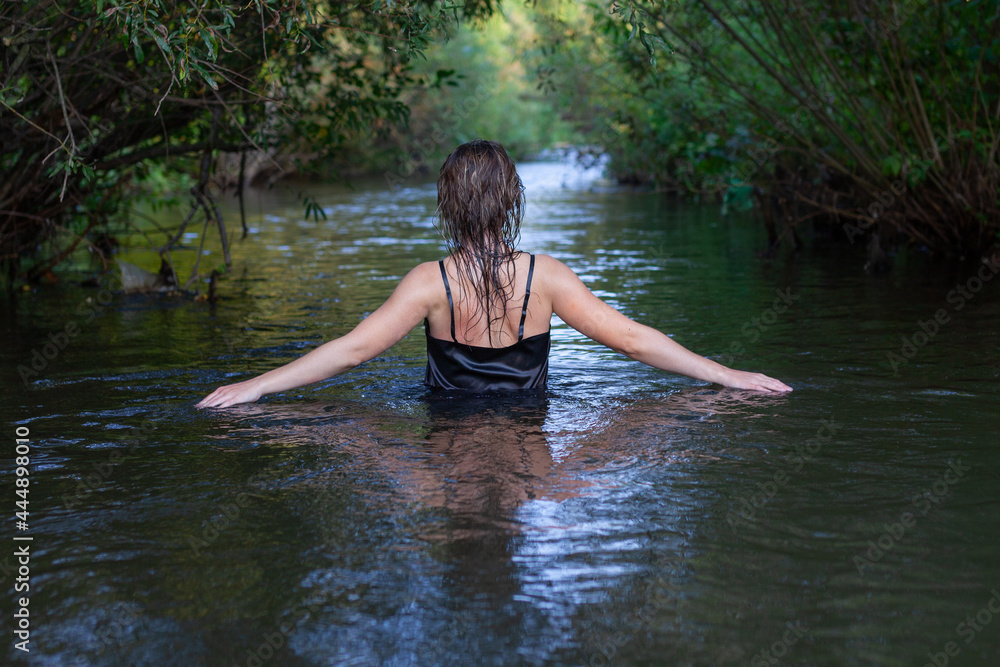 Fototapeta premium mystical woman in black dress splashes in the river