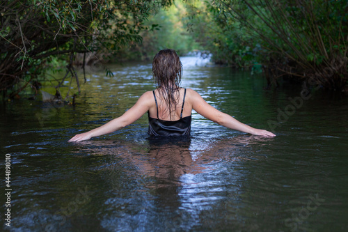 Fototapeta Naklejka Na Ścianę i Meble -  mystical woman in black dress splashes in the river