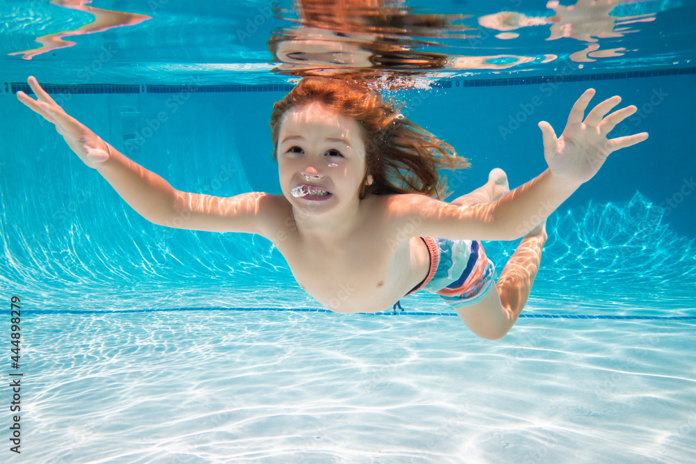 Child swims underwater in swimming pool, happy active boy dives and has fun under water, kids watersport. Summer activity. Healthy kids lifestyle. Summer vacation with children in a tropical resort.