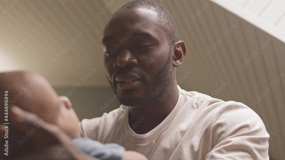 Low angle of loving young father sitting at home, looking at unrecognizable baby, swaying him on hands in front Low angle of loving young father sitting at home, looking at unrecognizable baby, swaying him on hands in front