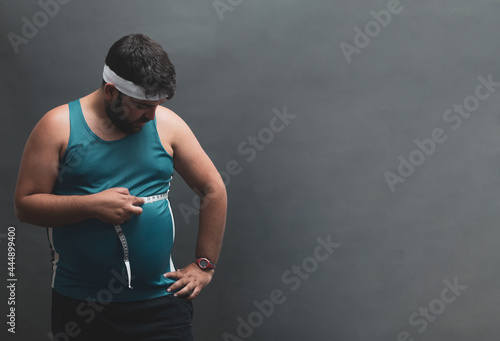 
fat young man measuring his belly with a tape measure. photo