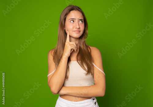Portrait of a pensive casual girl looking away at copy space isolated over green background © Danko