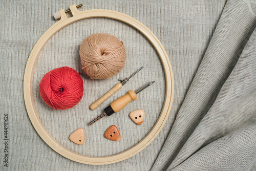 Layout of necessary things for cretive embriodery: stretching hoop, punch needles, balls of yarn and wooden buttons on textured linnen fabric. Hand made hobbies concept. photo