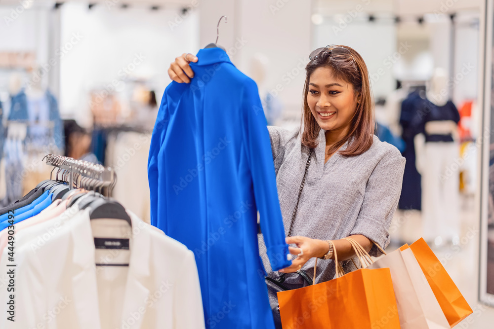 Happy Asian woman choosing clothes in glass store shop with happy action at department center, shopping and shopaholic, lifestyle fashion and leisure, sales and black friday concept