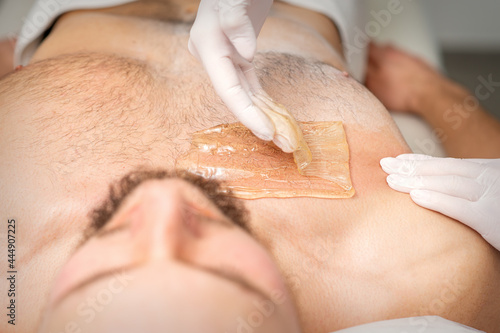 Young caucasian man receiving hair removal from his chest in a beauty salon, depilation men's torso photo