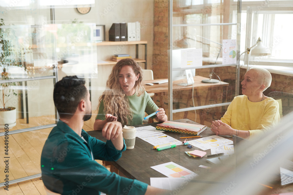 Group of business people sitting at the table and discussing in team during meeting at office behind the glass Group of business people sitting at the table and discussing in team during meeting at office behind the glass