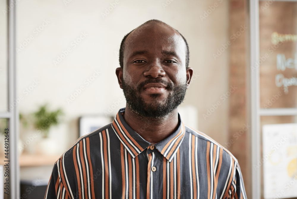 Portrait of African bearded man in striped shirt smiling at camera while standing at office