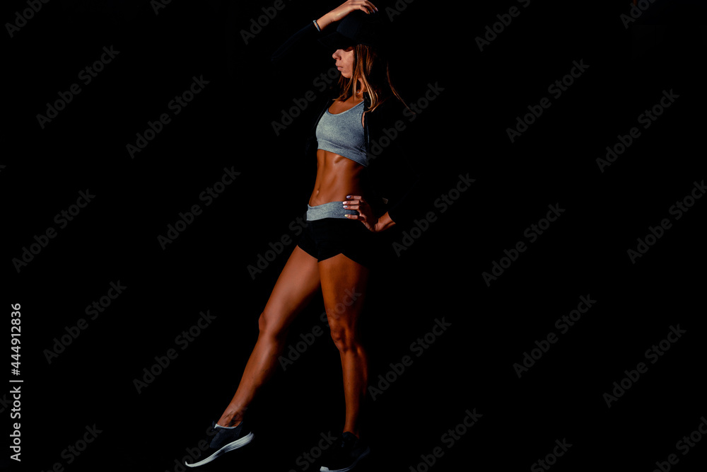 An attractive woman flexing her back on a black background. Sexy fitness model in a dark studio while covered in sweat after her training.