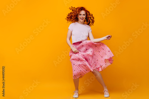 Young woman in midi skirt and cropped t-shirt jumping and dancing on orange background