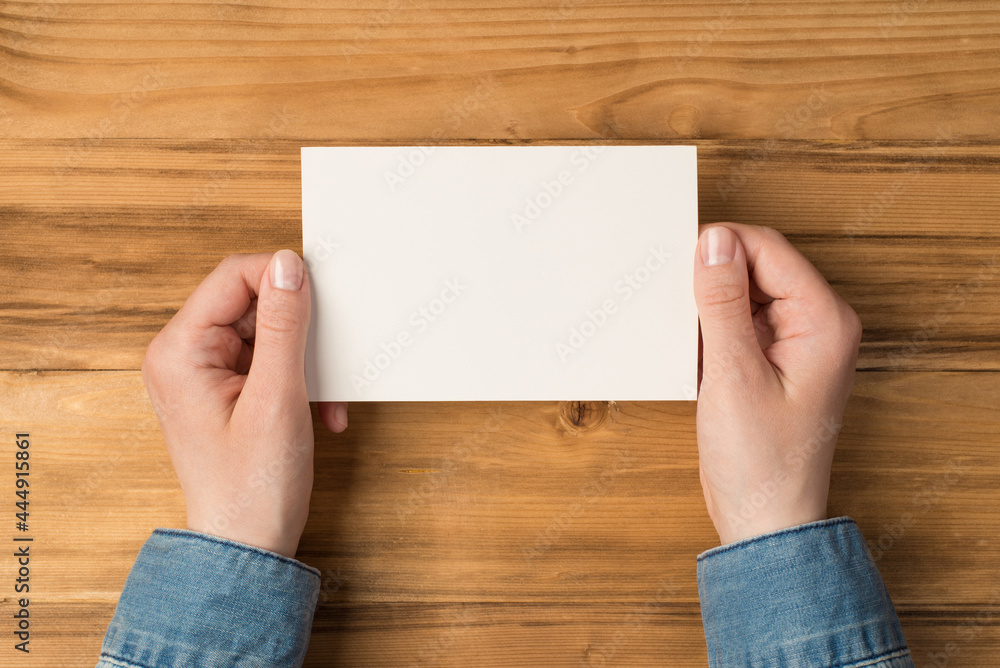First person top view photo of hands holding white paper card on isolated  wooden table background with blank space Stock Photo | Adobe Stock