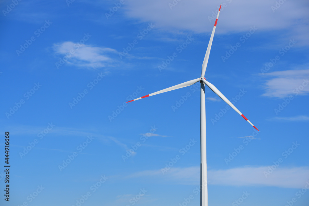 In front of a blue sky with clouds there is a large wind turbine for generating electricity with space for text