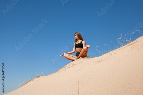 woman in sportswear doing yoga on the sand in the desert in the summer