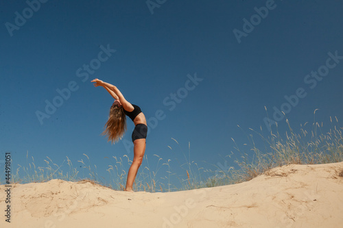 woman in sportswear doing yoga on the sand in the desert in the summer