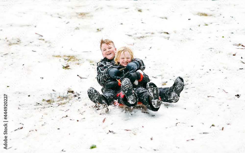 Obraz premium Two boys sharing a toboggan speeding down hill having a great time in the snow