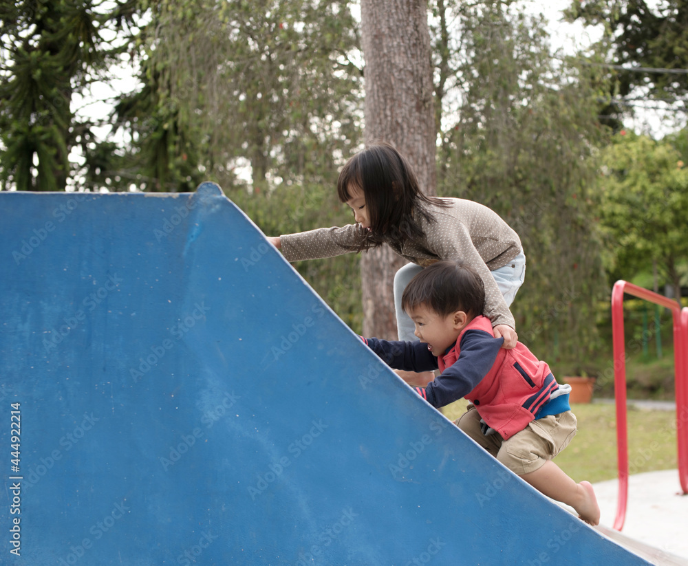 Older Malaysian child helping younger child up the ramp while playing ...