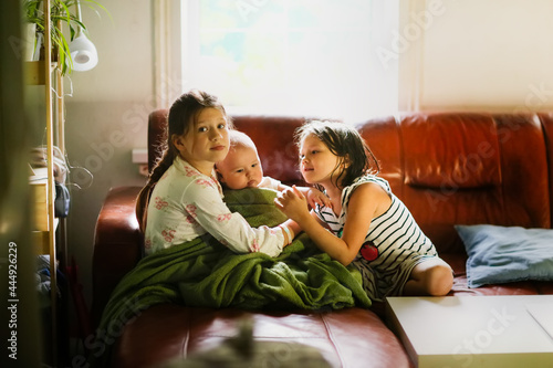 Cute kids siblings sisters with baby on ivan in the living room, dark style. Sibling relationship concept and family values, soft focus and blur © natalialeb