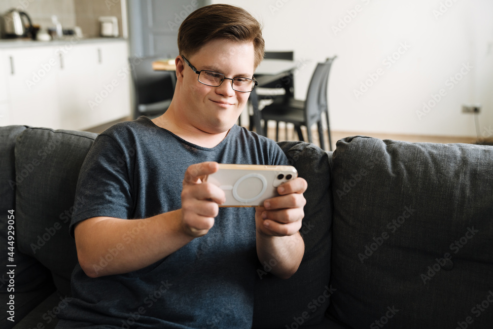 Young man with down syndrome using cellphone while sitting on couch Young man with down syndrome using cellphone while sitting on couch