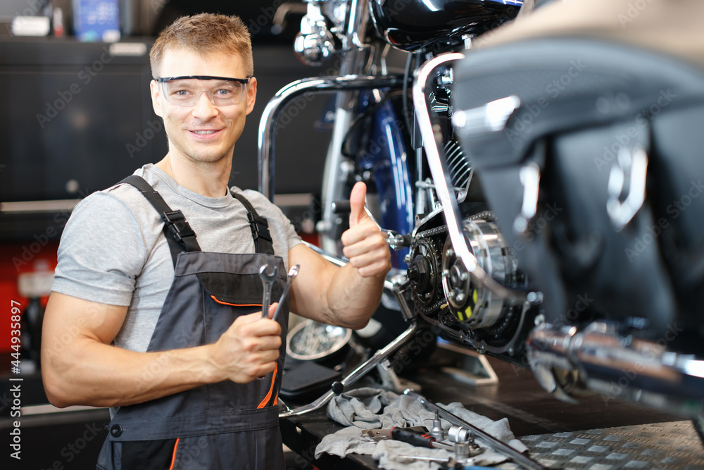 Motorcycle repair technician holds thumbs up while standing in workshop Motorcycle repair technician holds thumbs up while standing in workshop