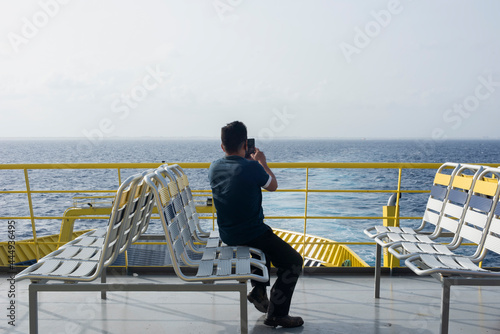A man with his back turned, sitting in a ro-ro ferry talking on the phone looking at the horizon over the sea. Cozumel Island, Mexico