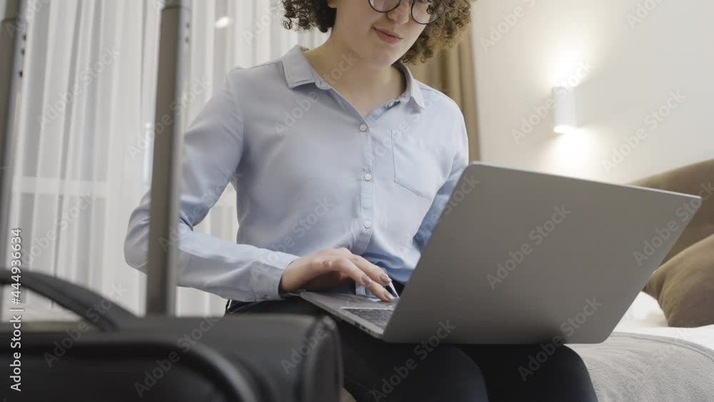 Curly-haired smiling woman working on laptop in hotel room, business trip time Curly-haired smiling woman working on laptop in hotel room, business trip time