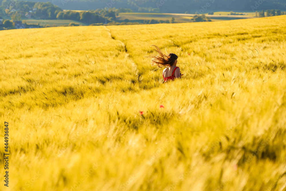 Pretty teenager girl with long hair enjoying nature running through  yellow barley field in countryside at sunny summer day. Healthy holidays lifestyle.