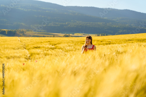 Pretty teenager girl with long hair enjoying nature at sunny summer day in yellow barley field in countryside. Healthy holidays lifestyle.