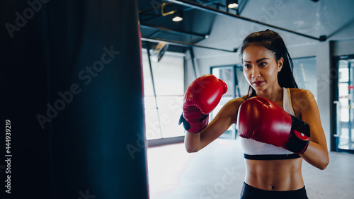 Young Asia lady kickboxing exercise workout punching bag tough female fighter practice boxing in gym fitness class. Sportswoman recreational activity, functional training, healthy lifestyle concept. © tirachard