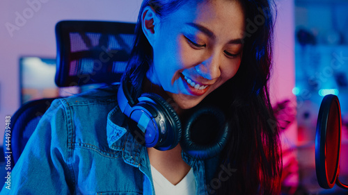 Fényképezés Happy asia girl blogger play synthesizer keyboard wear headphone and record music with sound mixer on laptop in living room home studio at night