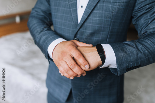 A man, a businessman, a director in a blue plaid suit, holds his arms crossed and looks at a black smart watch. Photography, concept.