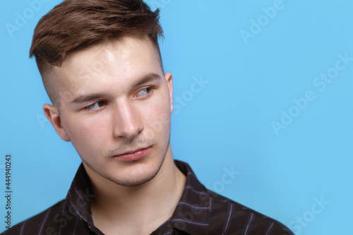 Closeup portrait of young handsome man with sidelong glance at right side. Trendy hairstyle, short accurate beard, classic official wear. Blue background, copy space for any text or objects.