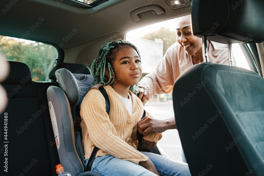 Black woman smiling while putting her daughter in child seat at car