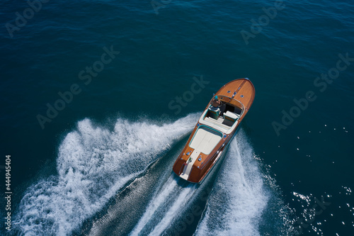 Classic Italian wooden boat fast moving aerial view. Top view of a wooden powerful motor boat. Luxurious wooden boat fast movement on dark water. © Berg