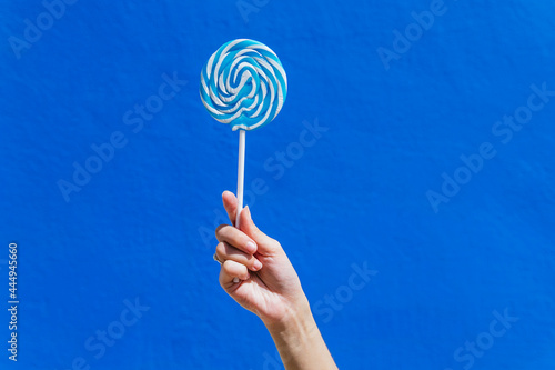Crop woman with sweet lollipop on blue background