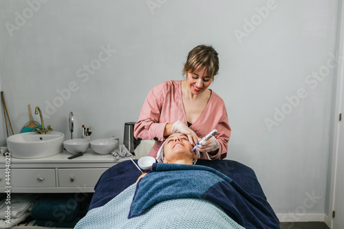 Cosmetologist doing microdermabrasion procedure of face of client photo