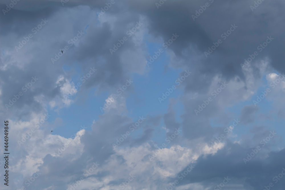 In the blue sky, gray rain clouds are crawling over the white clouds.