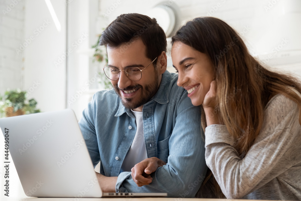 Beautiful millennial couple sit indoor have fun use laptop watch videos on-line, enjoy video call communication with friends spend carefree time together at home. Modern tech, e-commerce users concept Beautiful millennial couple sit indoor have fun use laptop watch videos on-line, enjoy video call communication with friends spend carefree time together at home. Modern tech, e-commerce users concept